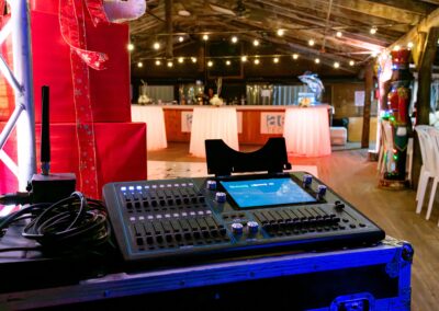 DJ mixing console with cables in the foreground, red decor and string lights overhead in a festive venue with a bar in the back